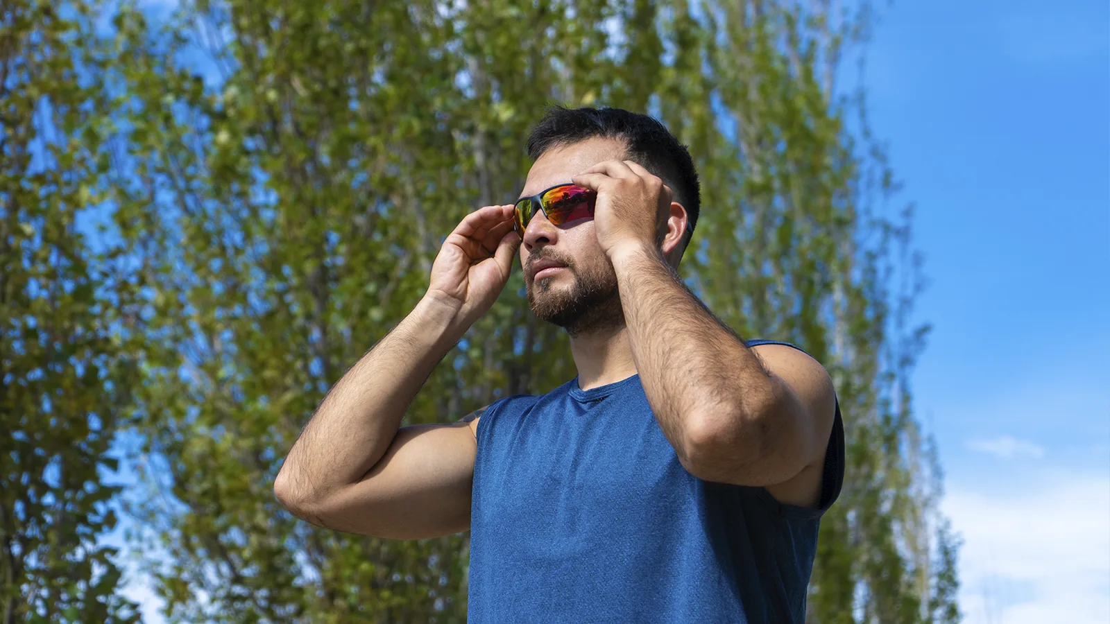 Hombre ajustándose unas gafas deportivas de lentes espejados al aire libre